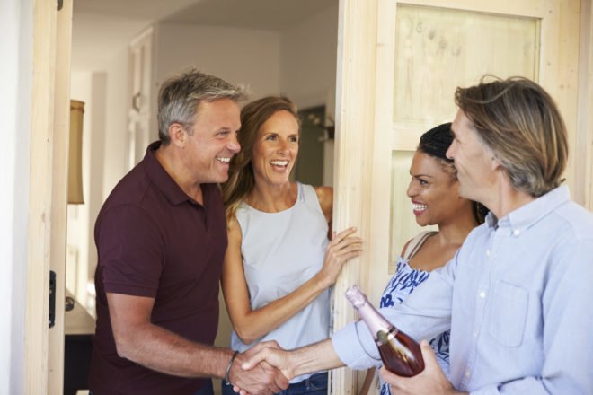 couple with bottle of wine greeting another couple