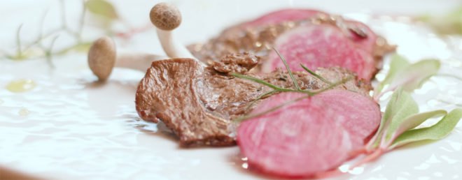 cooked lab grown meat placed on a white plate with garnishes and mushrooms