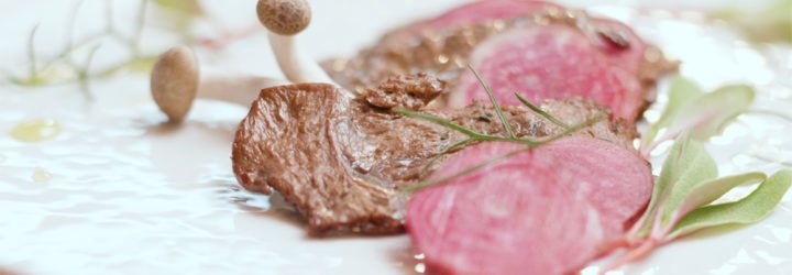 cooked lab grown meat placed on a white plate with garnishes and mushrooms