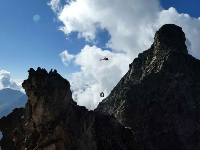 helicopter placing piece of bivouac on mountainside