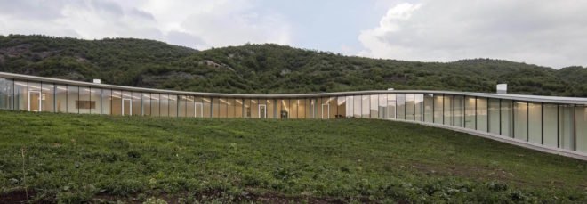 long, curving glass building on grassy hill