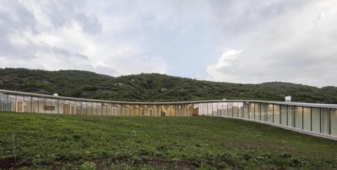 long, curving glass building on grassy hill