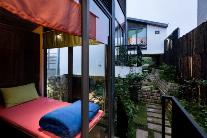 small bed with vibrant red sheets is near a large window overseeing the surrounding greenery on the property