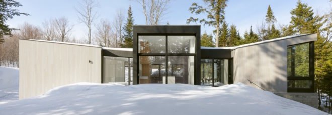 minimalist home with large windows surrounded by snow and trees