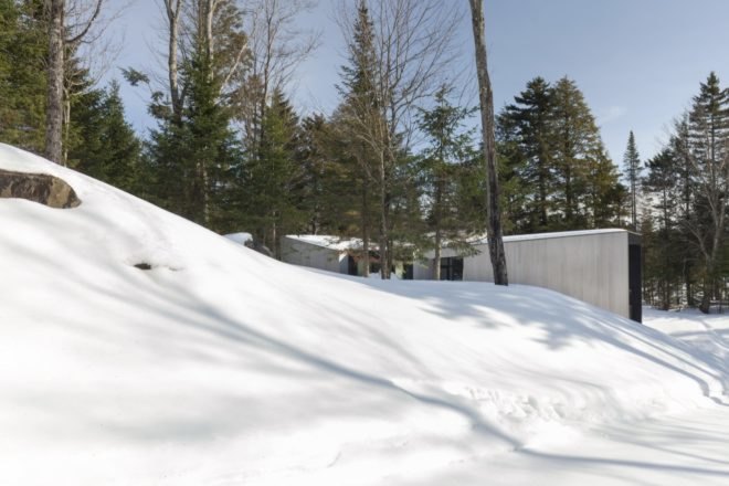 minimalist home with large windows surrounded by snow and trees