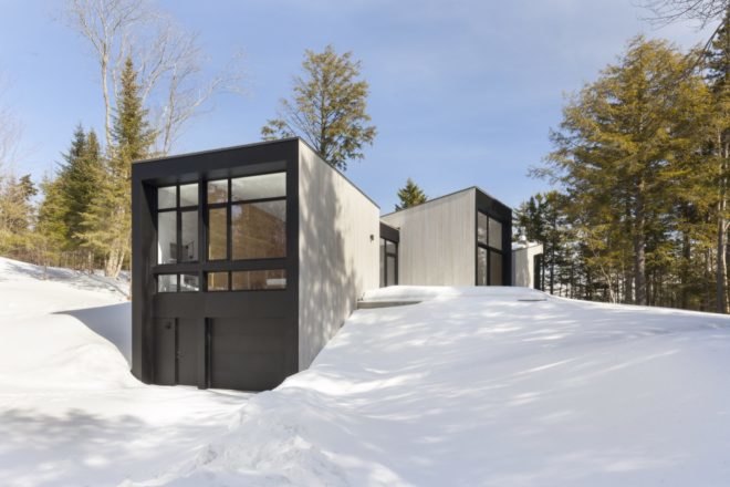 minimalist home with large windows surrounded by snow and trees