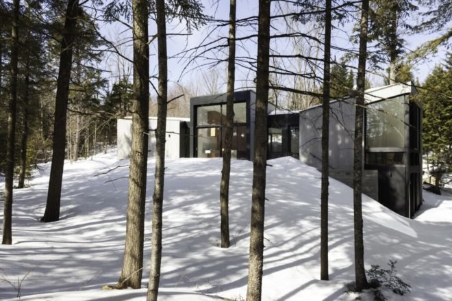 minimalist home with large windows surrounded by snow and trees