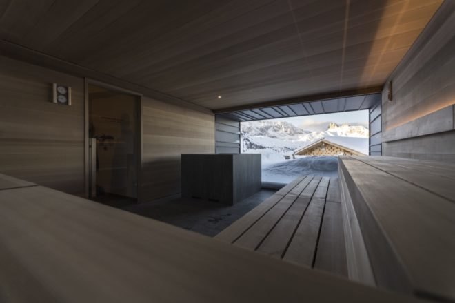 interior of chalet with sauna near a large window with snow covered mountains in background