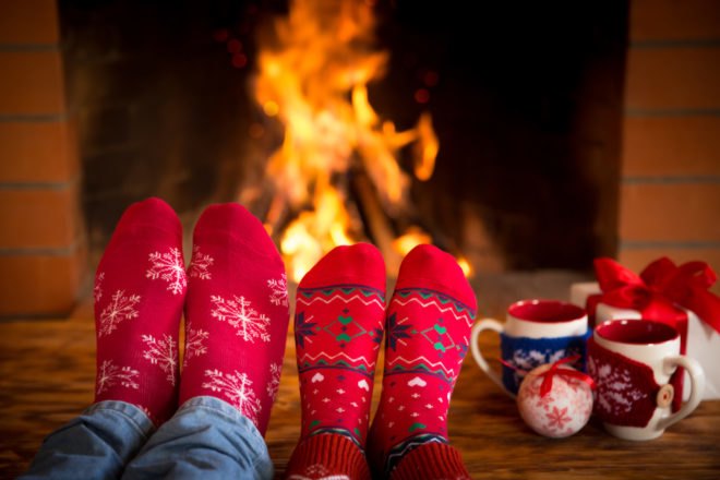 two pairs of feet in red socks near fire with mugs and gifts to the side