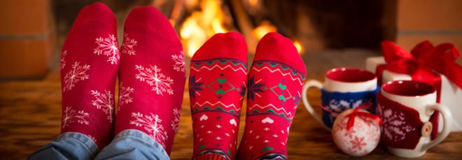 two pairs of feet in red socks near fire with mugs and gifts to the side