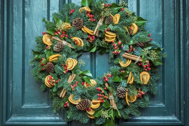 green wreath with pinecones and dried fruit on a green door