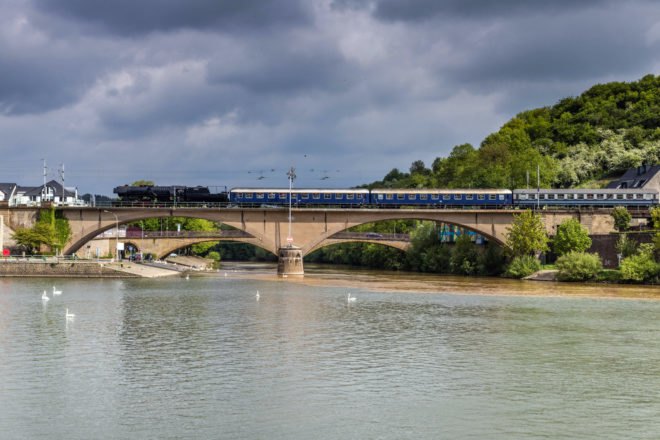 blue train on a bridge above a river