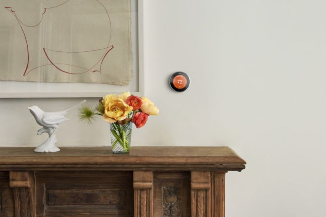 Nest smart thermostat on a wall beside a painting