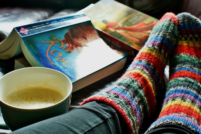 person wearing rainbow knit socks with a cup of coffee and books near feet