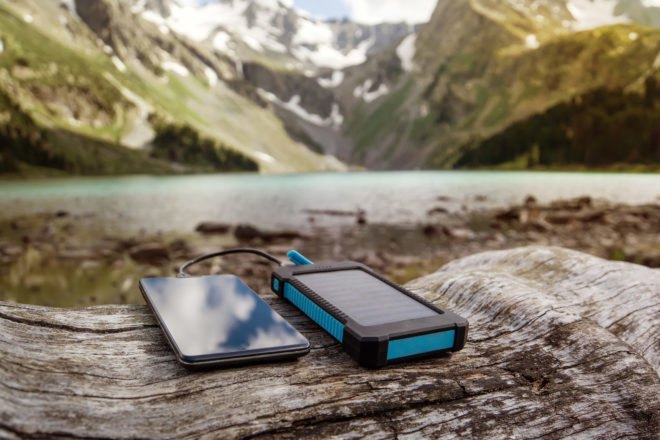 phone and solar-powered phone charger on a log with mountains in background
