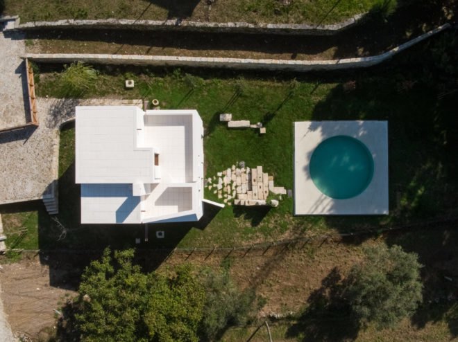 bird's eye view of white home with pool surrounded by greenery