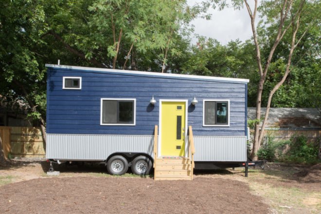 a tiny home on wheels with blue cladding and yellow door