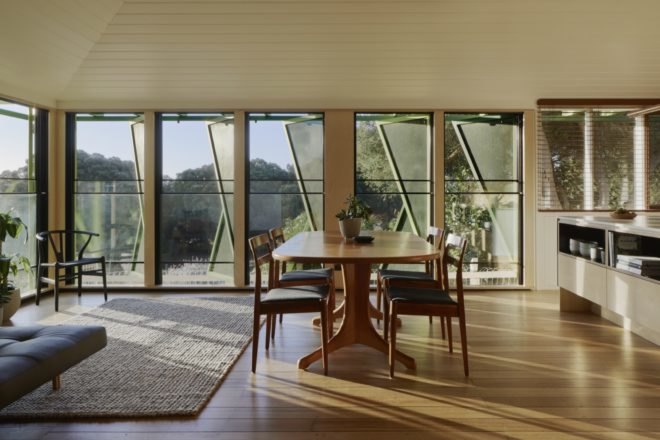 wood floors line the dining and living area of the home with a wood table and outside views from the shutter