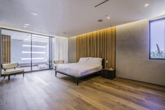 large bedroom with cement walls with wood floor to ceiling headboard and large windows
