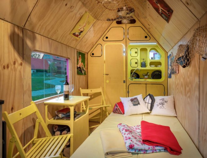 light wood-lined interior with small couch pulled out into a bed and two chairs