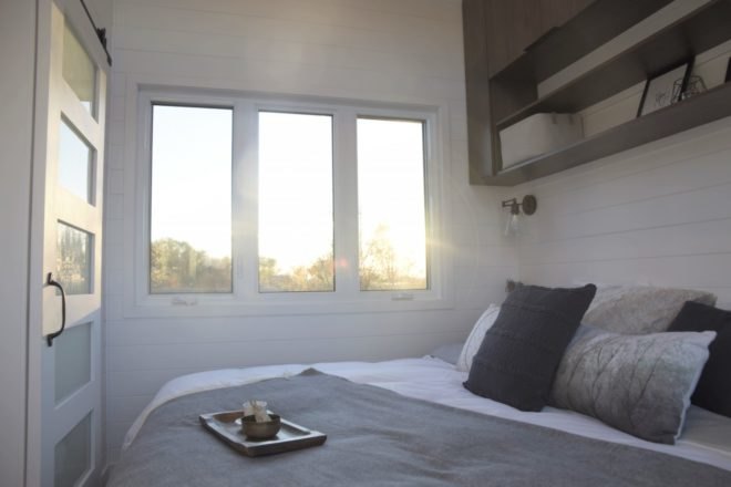bed with white and grey pillows and blankets and three windows