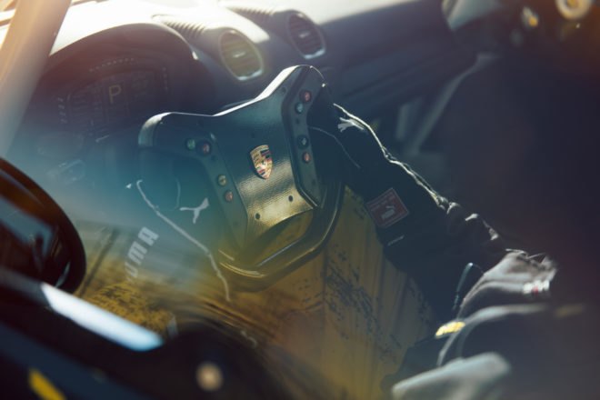 interior view of porsche cayman 's steering wheel with driver inside of vehicle