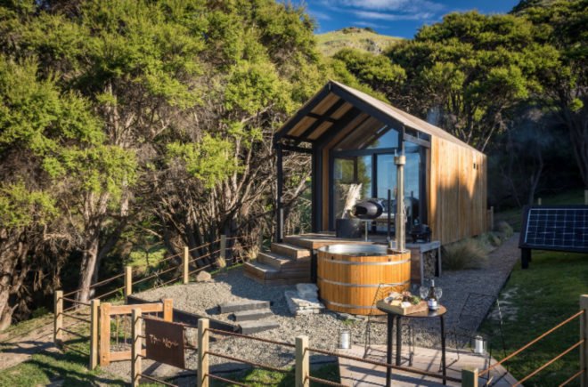 Tiny home with pitched roof, glass facade and wooden outdoor tub