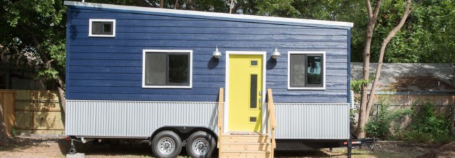 a tiny home on wheels with blue cladding and yellow door