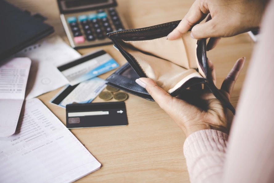 person opening empty wallet with credit cards, calculator and paper in the background