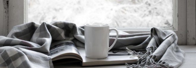 white coffee cup, book and blanket in front of window