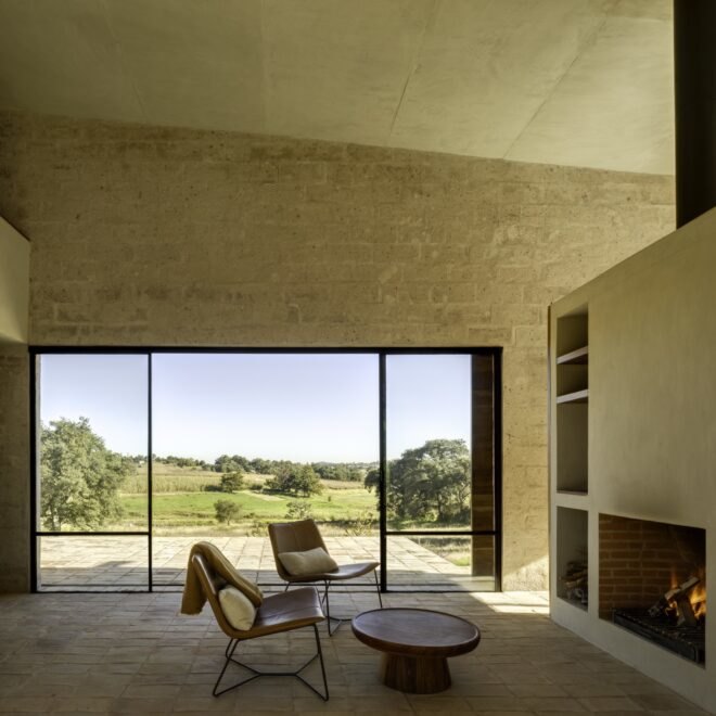 two chairs facing a shelving unit and fireplace with large windows on the side wall