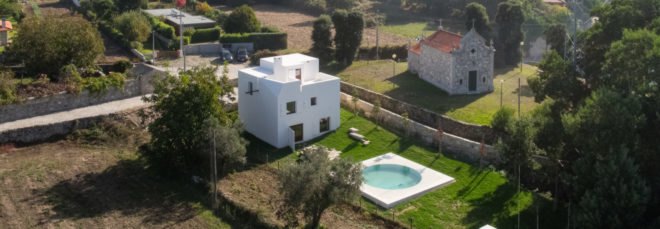 aerial view of white home with pool surrounded by greenery