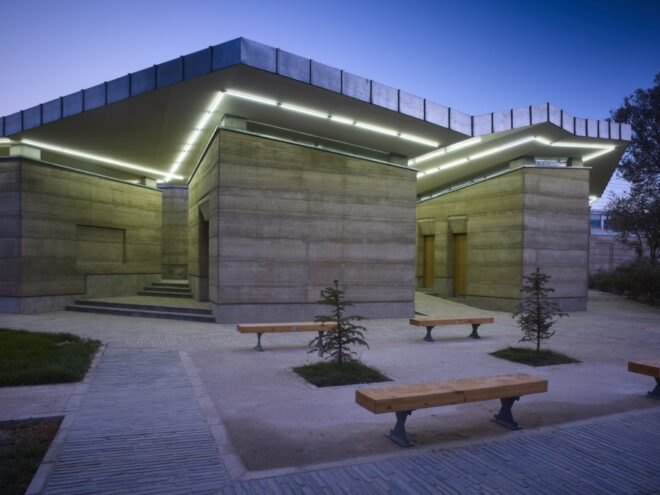 rammed earth building with green lighting and outdoor benches