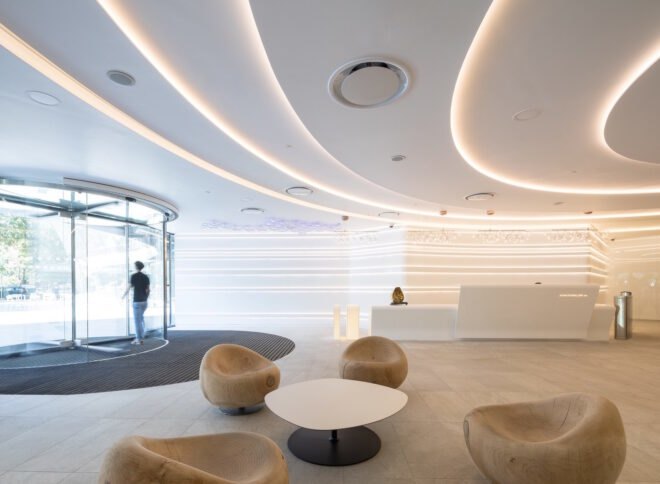 interior of building with white walls and ceiling light patterns with light brown colored seats around a white modern center table
