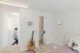 man walking past white room with bed and guitar