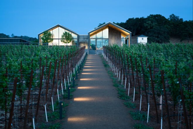 long extended building with gabled roof and rows of grapes growing in front of it
