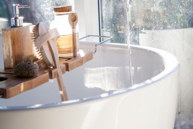 free-standing tub with wood bath caddy, bamboo brushes and glass jar of bath salts