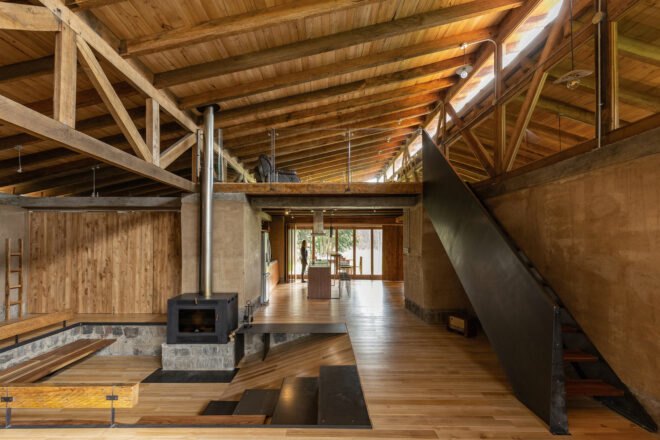 room with rammed earth walls and wood floors plus a wood-burning stove and stairs leading to higher floor