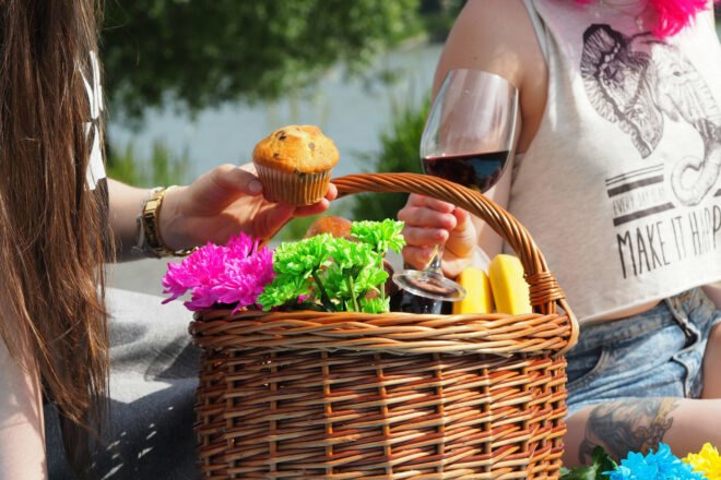 two people grabbing muffins and wine from a picnic basket