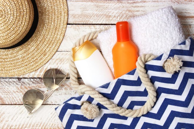 sunscreen bottles in a beach bag near a floppy straw hat