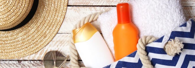 sunscreen bottles in a beach bag near a floppy straw hat