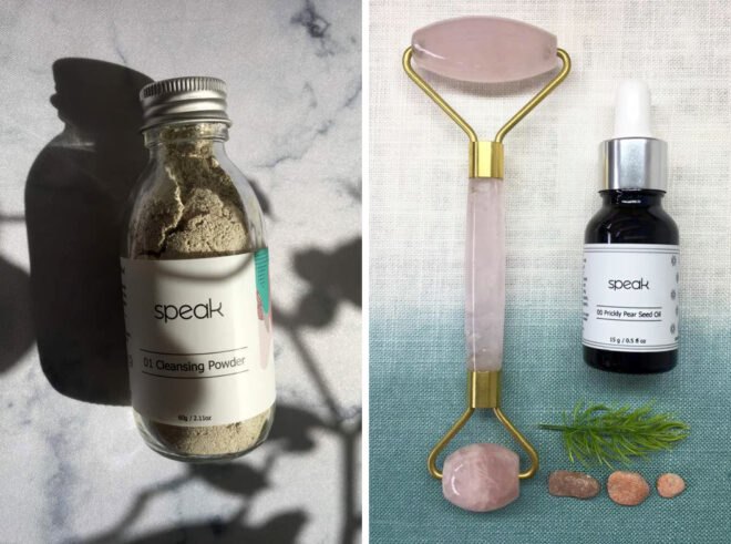 On the left, glass jar of cleansing powder. On the right, rose quartz roller and small vial of prickly pear seed oil.