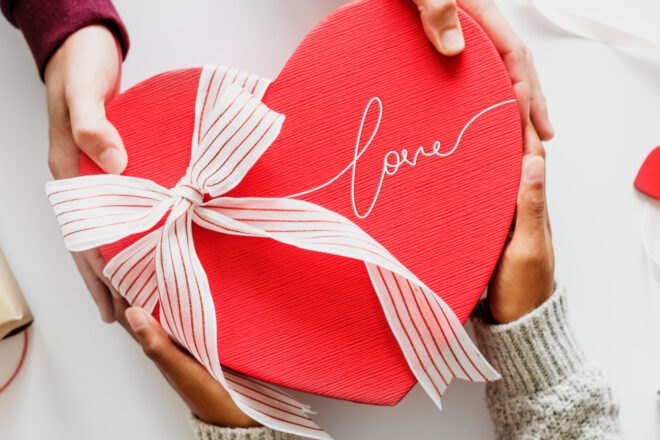 two sets of hands holding a red heart-shaped box