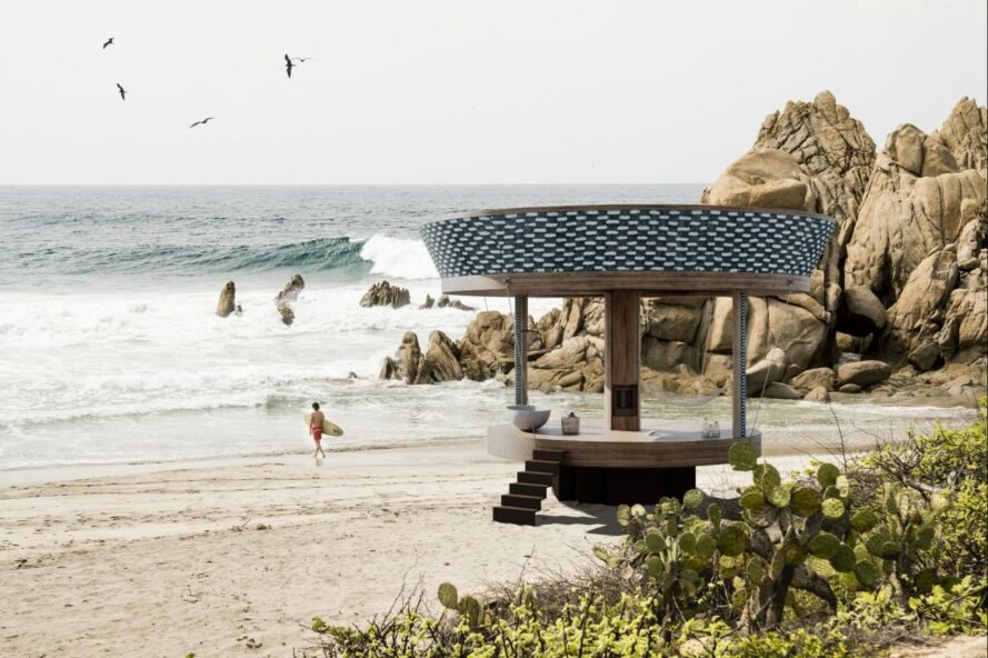 round structure on beach with surfer walking by