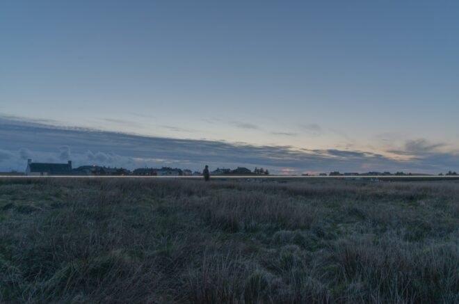 man walking in field next to long white LED light
