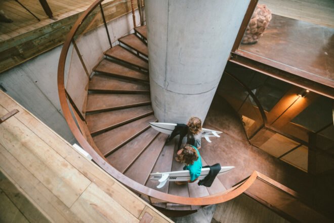 two people carrying surf boards walking up a flight of stairs