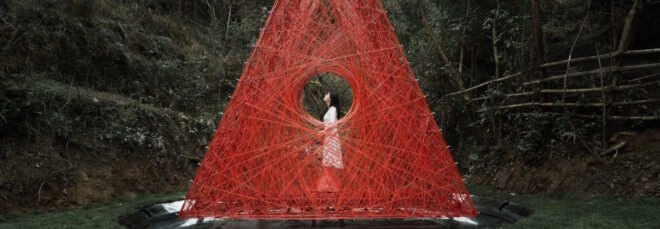 woman standing inside red woven triangle pavilion