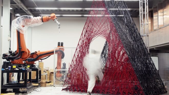 person testing strength of red carbon-fiber pavilion in a lab