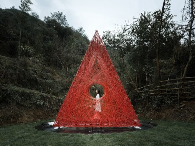 woman standing inside red woven triangle pavilion