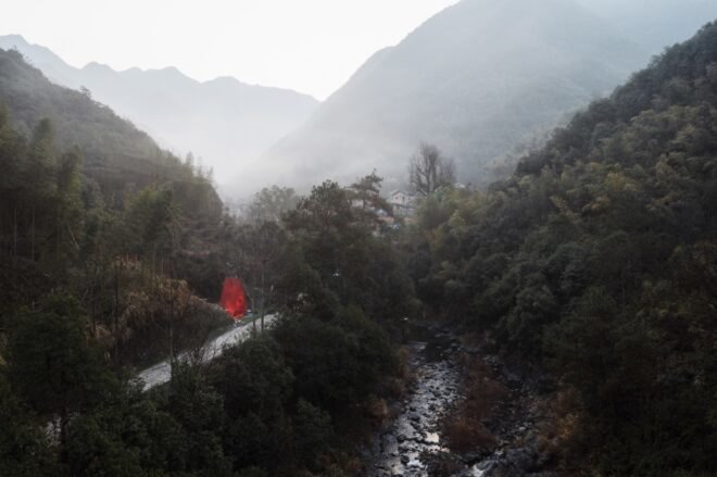 red triangular pavilion on a hillside with mountains in the background